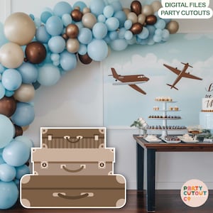 May include: A stack of three brown suitcases with vintage style handles and buckles. The suitcases are in front of a blue and white balloon arch and a dessert table with a cake that says "Let's  we the  Mini".