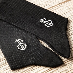May include: A pair of black socks with white pinstripes and a white embroidered letter "S" on each sock.