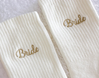 May include: A pair of white socks with the word "Bride" embroidered in gold on each sock.