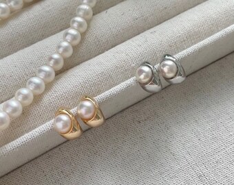 May include: A pair of pearl earrings in gold and silver settings. The earrings are displayed on a white fabric surface with a pearl necklace.