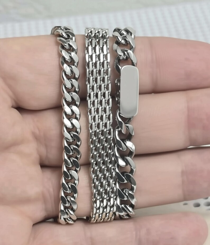 A person's hand holding three silver-colored metal bracelets.