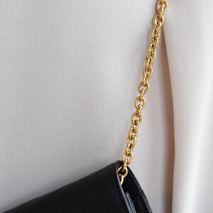 A close-up view of a black leather handbag with a gold chain strap, worn on a person's arm.