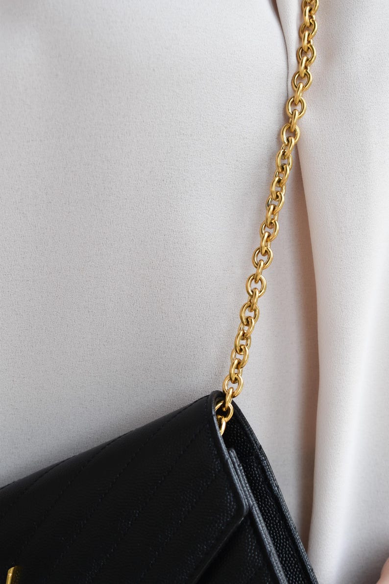 A close-up view of a black leather handbag with a gold chain strap, worn on a person's arm.