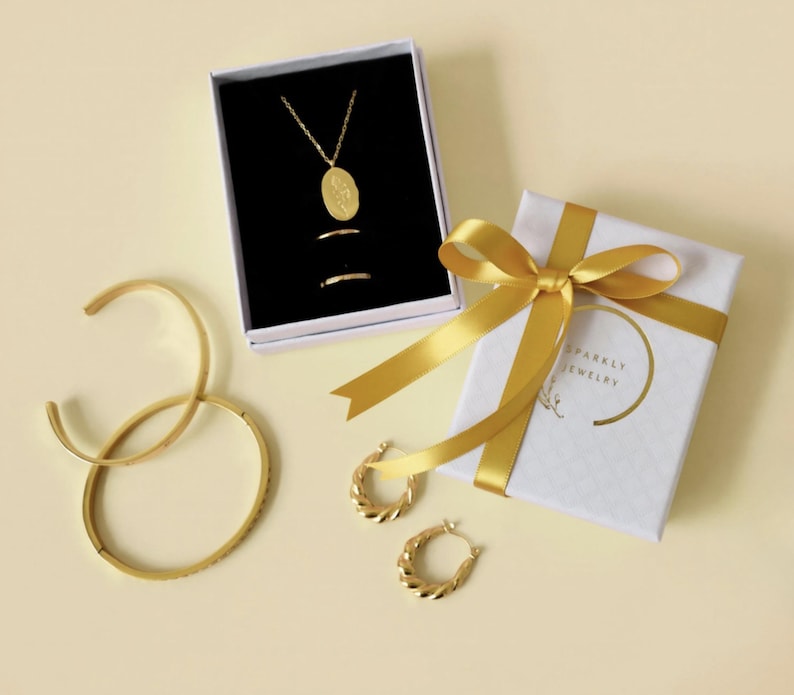 a collection of gold jewelry and accessories, including a necklace, earrings, bracelets, and a gift box with a ribbon.