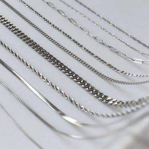 a collection of various silver chain necklaces arranged in a row.