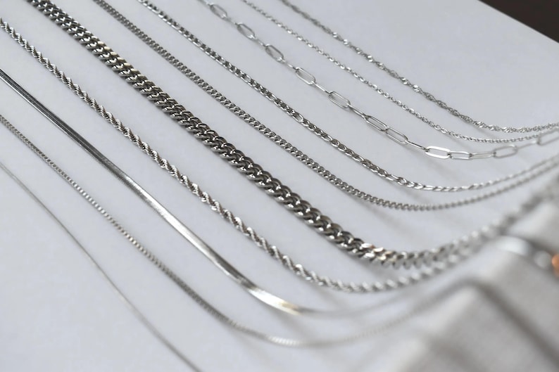 a collection of various silver chain necklaces arranged in a row.