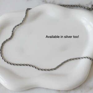 A silver necklace chain is displayed on a white plate, with the text "Available in silver too!" written on the plate.