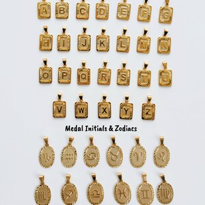 a collection of gold-colored pendants in the shape of letters and zodiac signs, arranged in rows and columns.