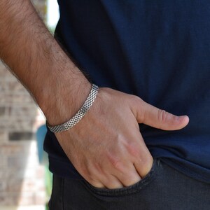 A close-up view of a person's hand wearing a silver bracelet, with their hand resting in their pocket.