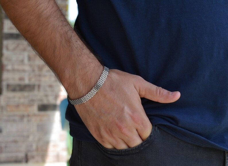 A close-up view of a person's hand wearing a silver bracelet, with their hand resting in their pocket.