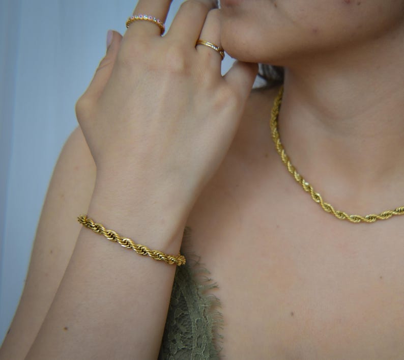 A close-up of a person's hand wearing a gold bracelet and necklace, with a focus on the bracelet and necklace.