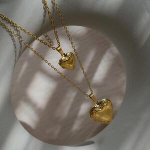 A gold heart-shaped pendant necklace with two smaller heart-shaped pendants hanging from it, set against a white circular background.