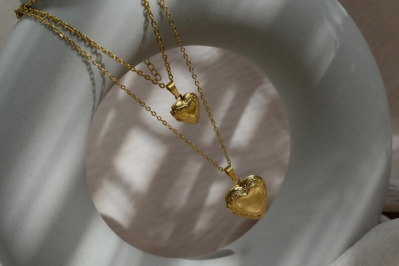 A gold heart-shaped pendant necklace with two smaller heart-shaped pendants hanging from it, set against a white circular background.