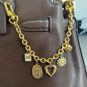 A close-up view of a brown leather handbag, showcasing a gold chain and various charms attached to it.