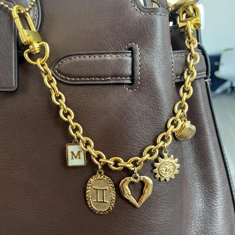 A close-up view of a brown leather handbag, showcasing a gold chain and various charms attached to it.