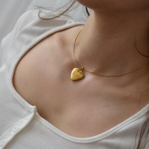 A close-up view of a woman's neck and chest area, showing a gold heart-shaped pendant necklace.
