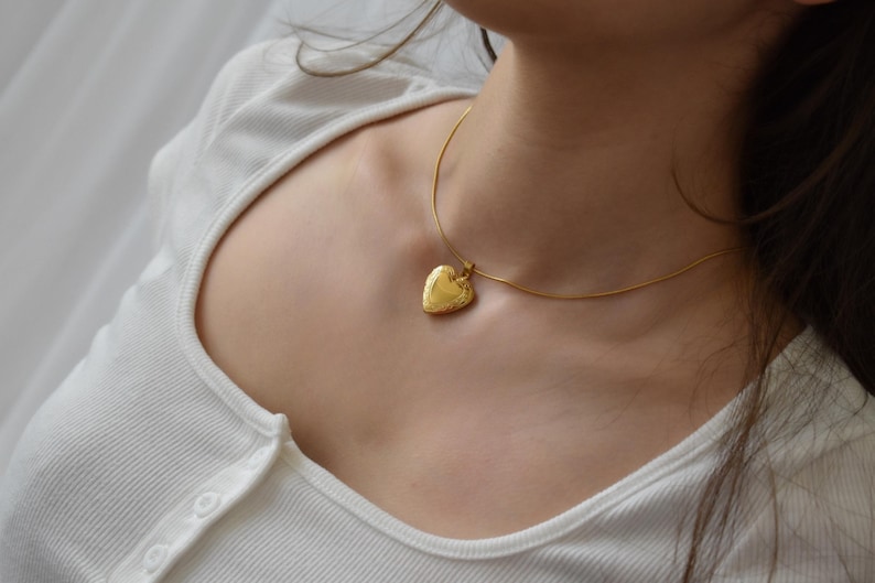 A close-up view of a woman's neck and chest area, showing a gold heart-shaped pendant necklace.