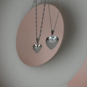Two silver heart-shaped pendants hanging from a chain against a white circular background.