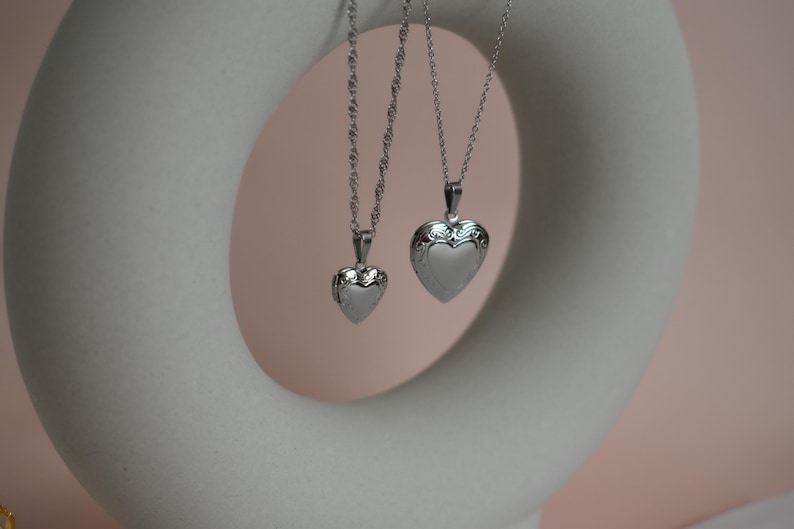 Two silver heart-shaped pendants hanging from a chain against a white circular background.