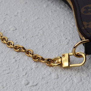 A close-up view of a gold chain strap and a gold clasp on a purse or bag.