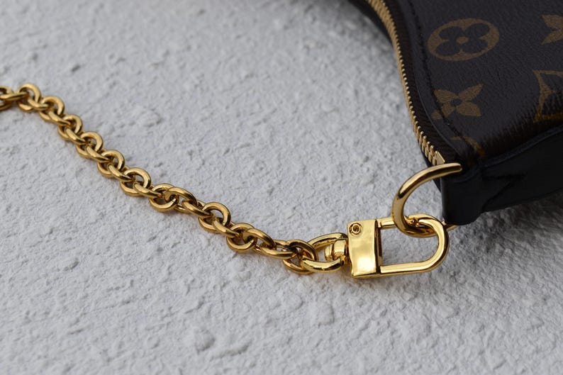 A close-up view of a gold chain strap and a gold clasp on a purse or bag.