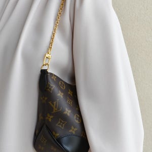 A person wearing a white blouse and carrying a small purse with a gold chain strap.