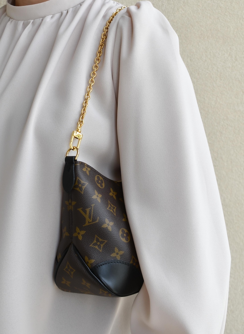 A person wearing a white blouse and carrying a small purse with a gold chain strap.