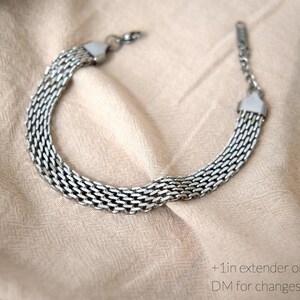 A silver chain bracelet with multiple links is displayed on a beige fabric background.