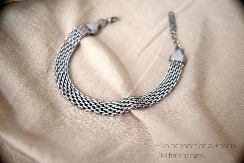 A silver chain bracelet with multiple links is displayed on a beige fabric background.