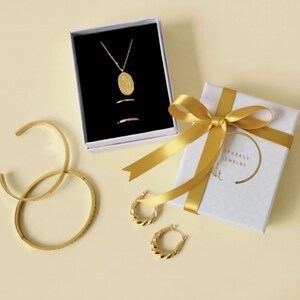 a collection of gold jewelry and accessories, including a necklace, earrings, bracelets, and a gift box with a ribbon.