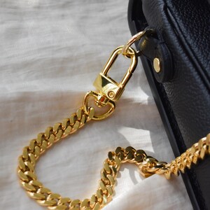 A close-up view of a gold chain strap and clasp on a black leather handbag.