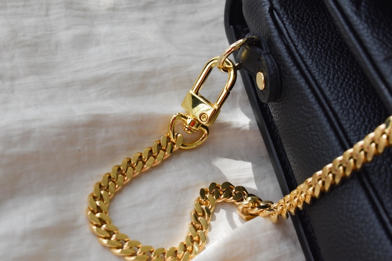 A close-up view of a gold chain strap and clasp on a black leather handbag.