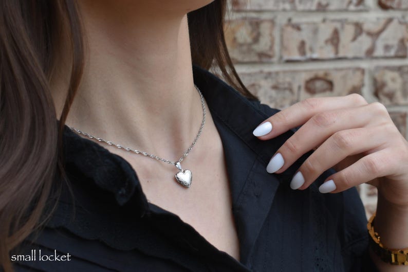 A close-up of a woman's neck and chest wearing a silver necklace with a heart-shaped pendant.