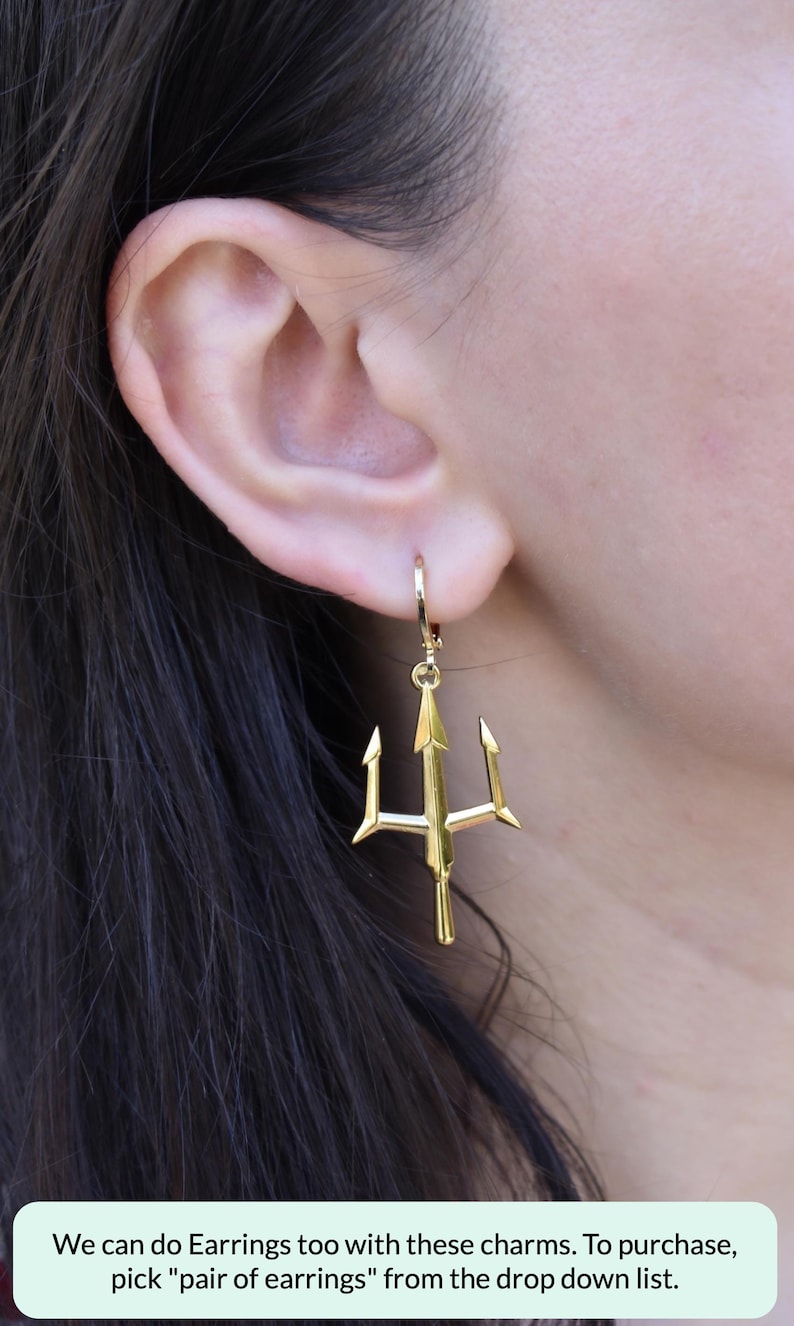 A close-up view of a person's ear wearing a pair of gold-colored earrings shaped like a trident.