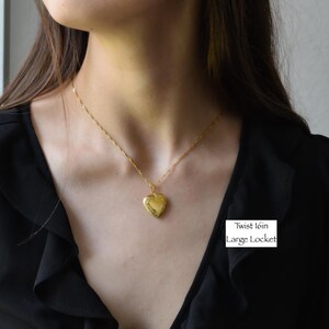 A woman wearing a black blouse with a gold heart-shaped locket necklace.