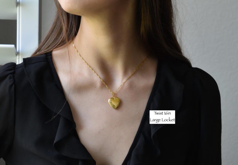 A woman wearing a black blouse with a gold heart-shaped locket necklace.