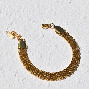 A gold-colored bracelet with a chain-like design is shown against a white background.