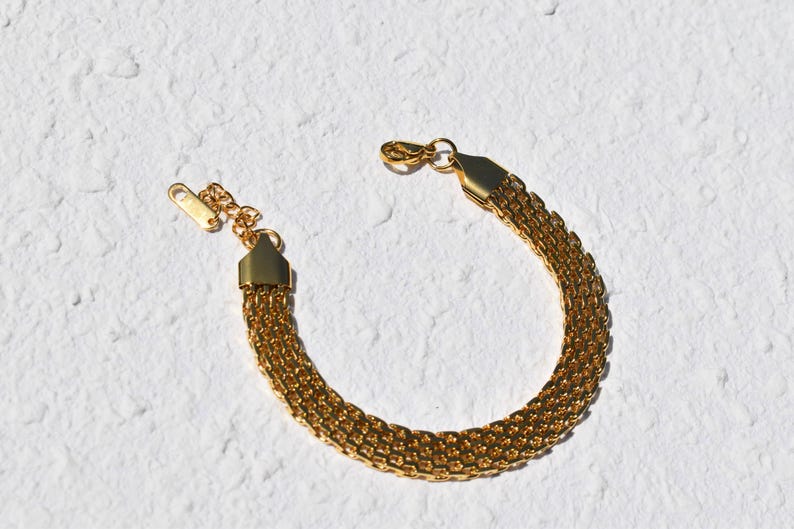 A gold-colored bracelet with a chain-like design is shown against a white background.
