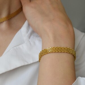 A close-up of a person's hand wearing a gold-colored bracelet and necklace.