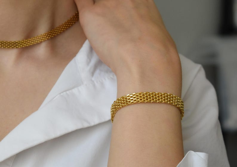 A close-up of a person's hand wearing a gold-colored bracelet and necklace.