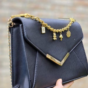 A hand holding a black leather handbag with gold chain accents and charms.