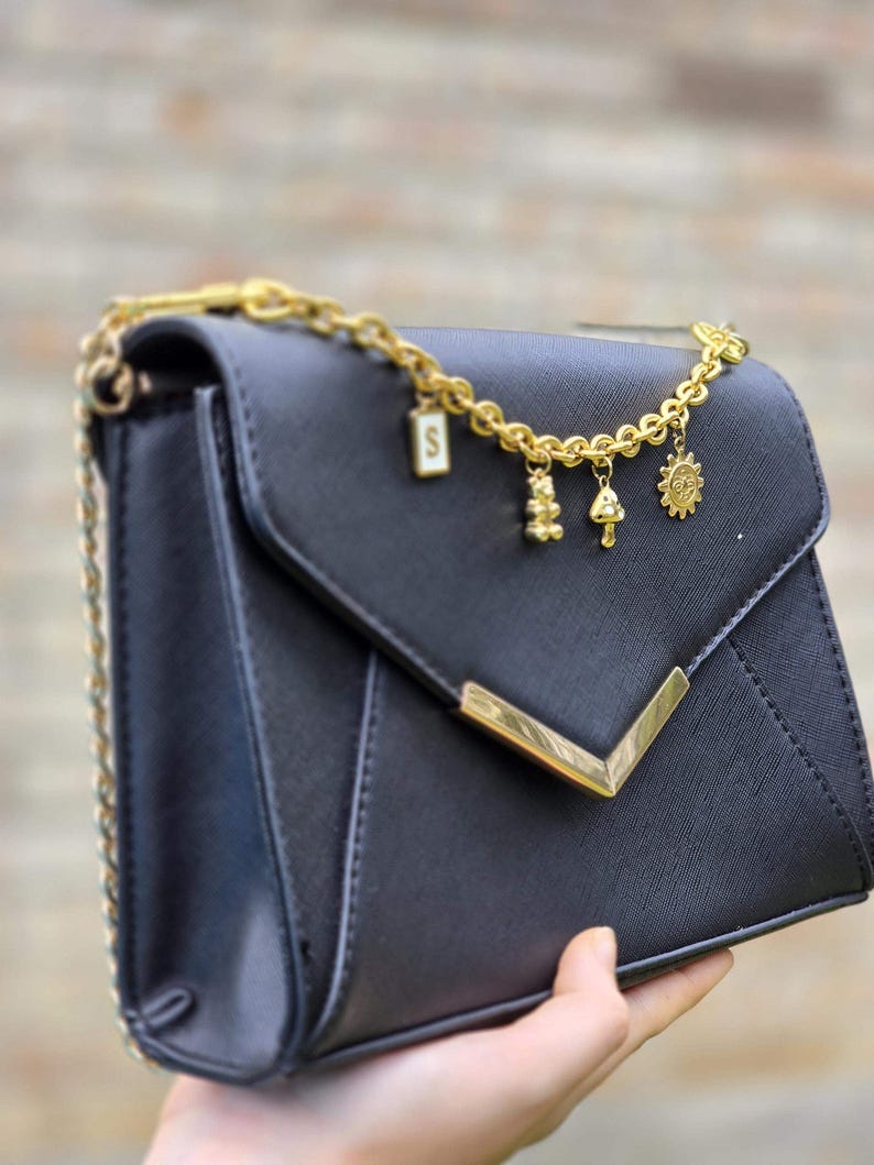 A hand holding a black leather handbag with gold chain accents and charms.