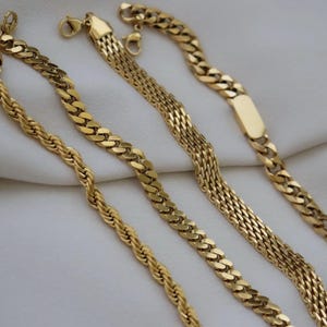 a collection of gold necklaces with various designs and lengths, arranged on a white background.