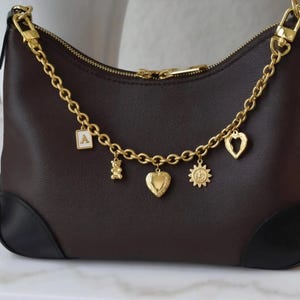 A brown leather handbag with gold chain accents and various charms attached to it.
