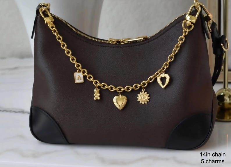 A brown leather handbag with gold chain accents and various charms attached to it.