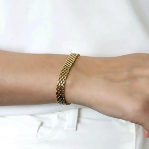 A gold bracelet is worn on a person's wrist.