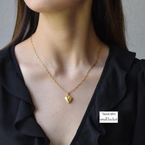 A woman wearing a black blouse with a gold necklace and a small heart-shaped pendant.