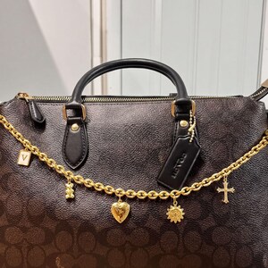 A black Coach handbag with gold accents, including a chain, charms, and a tag.