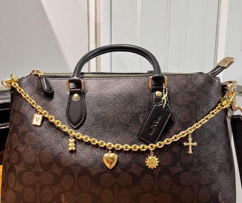 A black Coach handbag with gold accents, including a chain, charms, and a tag.