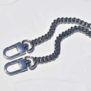 a pair of silver metal chain straps with lock-like attachments, lying on a white surface.